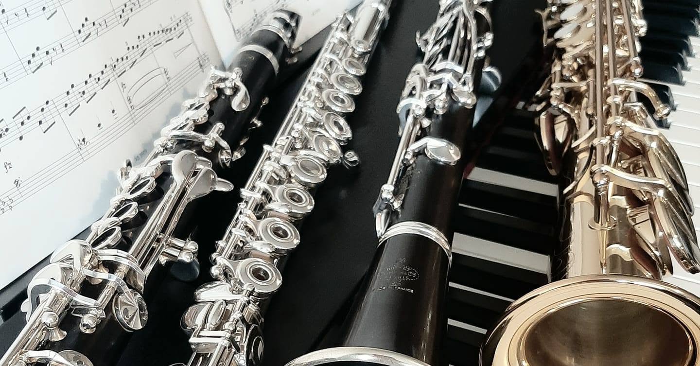Clarinets, a flute and a saxophone laid across a keyboard